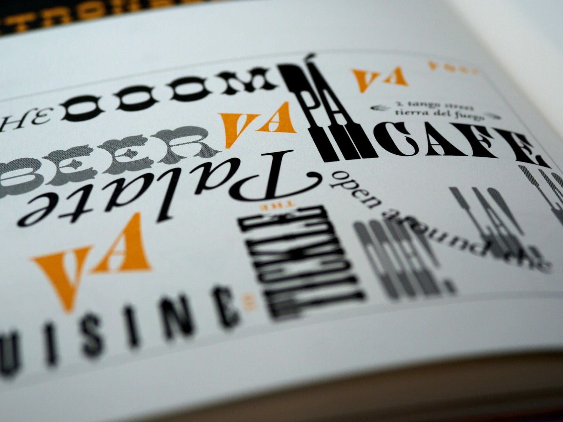 Close-up of a page with various text in different fonts, orientations, and sizes, primarily in black and orange. The words include "CUISINE," "CAFE," and "PALAIS." Some text appears upside down.
