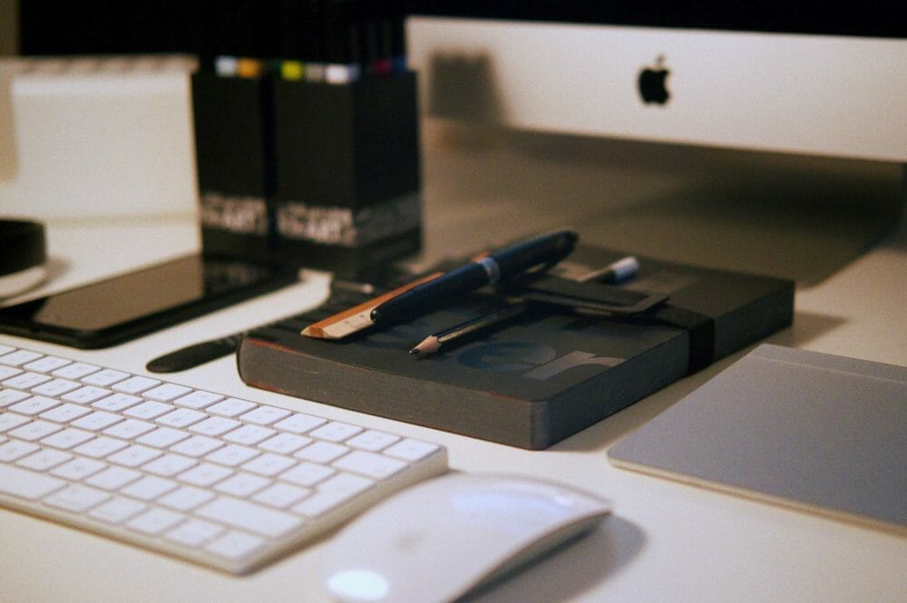 A neatly organized desk with a keyboard, mouse, notebook, pens, and an iMac computer.