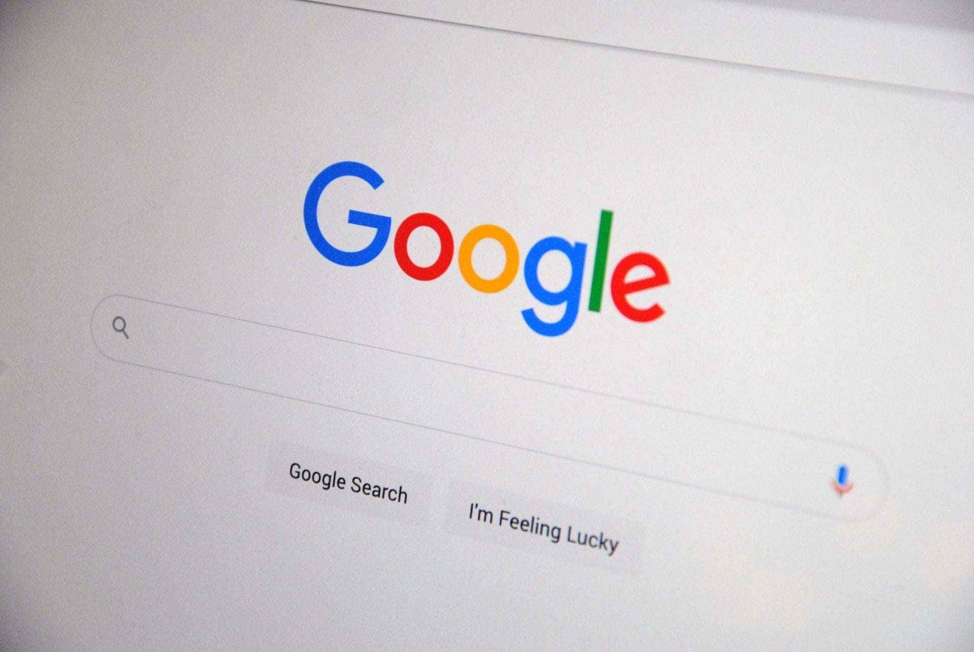 Google search engine homepage with Google logo, search bar, and two buttons labeled "Google Search" and "I'm Feeling Lucky." A microphone icon appears to the right of the search bar.
